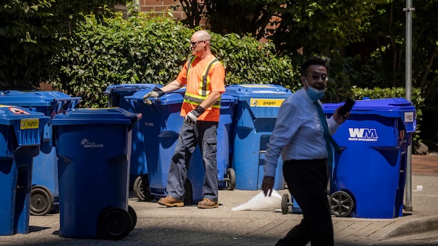 Isang waste collector ang nakatayo sa tabi ng kalsada katabi ang mga recycle bins.
