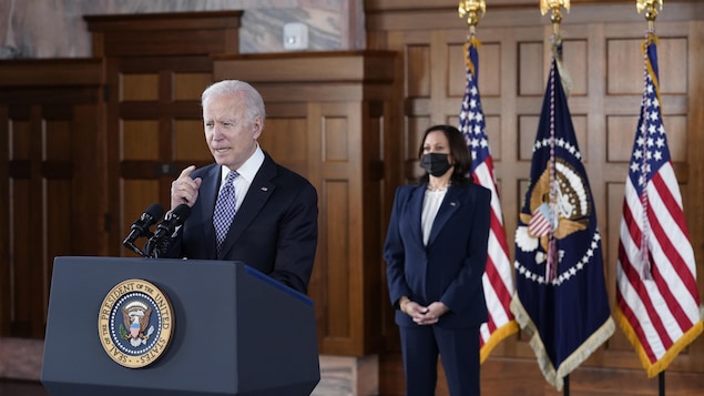 Joe Biden parle dans un micro tandis que Kamala Harris, qui porte un couvre-visage, se tient debout derrière lui.
