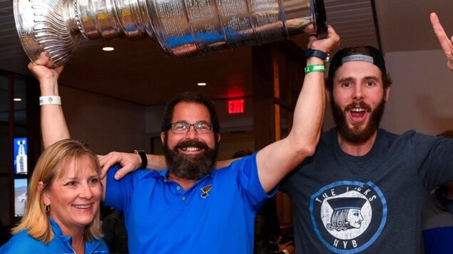 Le père de Joel Edmundson tient la coupe Stanley à bout de bras et affiche un large sourire. Il est accompagné de son fils et sa femme.