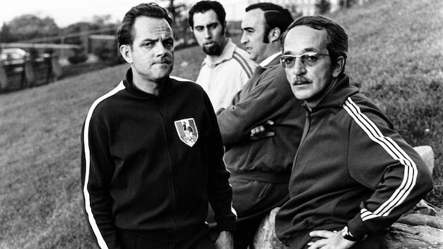 Jo Mallejac, Raymond Charette, Michel Charland et Raymond Beauchemin en survêtement de sport en pause sur une pente gazonnée.