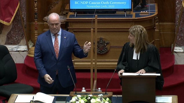 Le premier ministre donne un petit coup avec deux doigts sur le panneau de plexiglas dans la chambre de l'assemblée.
