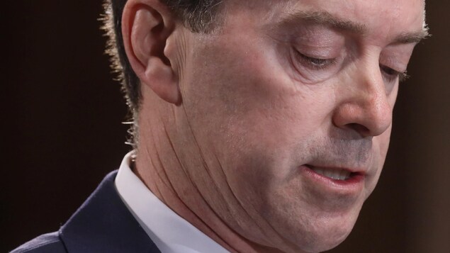 Gros plan de John Sanders, qui regarde vers le bas.