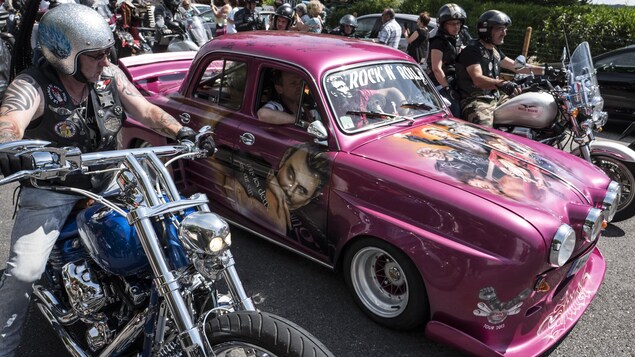 Des motards en convoi accompagne une voiture Renault Dauphine rose peinte avec des portraits du chanteur Johnny Hallyday sur une route. Des motards en convoi accompagne une voiture Renault Dauphine rose peinte avec des portraits du chanteur Johnny Hallyday sur une route.