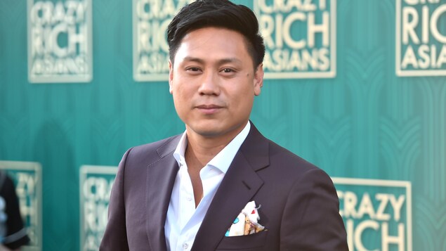 Le réalisateur Jon M. Chu regarde l'objectif de la caméra devant un grand panneau faisant la promotion du film « Crazy Rich Asians ». Le réalisateur Jon M. Chu regarde l'objectif de la caméra devant un grand panneau faisant la promotion du film « Crazy Rich Asians ».