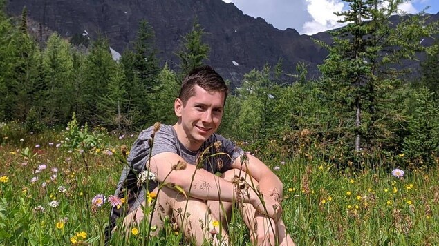 Photo du jeune Jordan Naterer assis dans l'herbe devant des montagnes rocheuses.