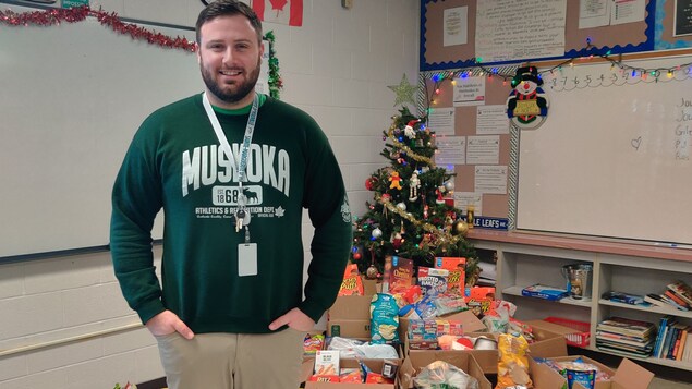 Un homme pose devant un arbre de Noël dans une salle de classe.