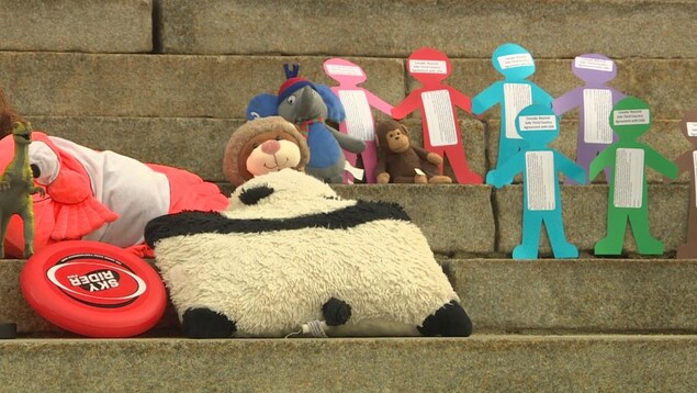 Sur des marches en béton, on voit des petites peluches en forme d'animaux et des papiers de différentes couleurs, découpés en forme de bonhommes qui se tiennent la main. Sur des marches en béton, on voit des petites peluches en forme d'animaux et des papiers de différentes couleurs, découpés en forme de bonhommes qui se tiennent la main.