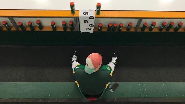 Un joueur de l'équipe de hockey junior des Broncos est assis seul sur son banc en écoutant de la musique et regarde la patinoire. Un joueur de l'équipe de hockey junior des Broncos est assis seul sur son banc en écoutant de la musique et regarde la patinoire.