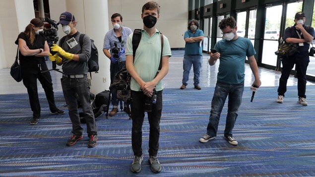 Des représentants des médias portant de l’équipement de protection comme des gants et des masques attendant dans un hall.