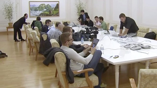 Des journalistes sont assis autour d'une table avec des ordinateurs portatifs et des téléphones cellulaires. Des Nord-Coréens sont debout autour de la table. . Des journalistes sont assis autour d'une table avec des ordinateurs portatifs et des téléphones cellulaires. Des Nord-Coréens sont debout autour de la table. .