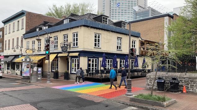 Une partie d'un trottoir peint aux couleurs du drapeau arc-en-ciel des communautés LGBTQ+ sur lequel marche des passants.