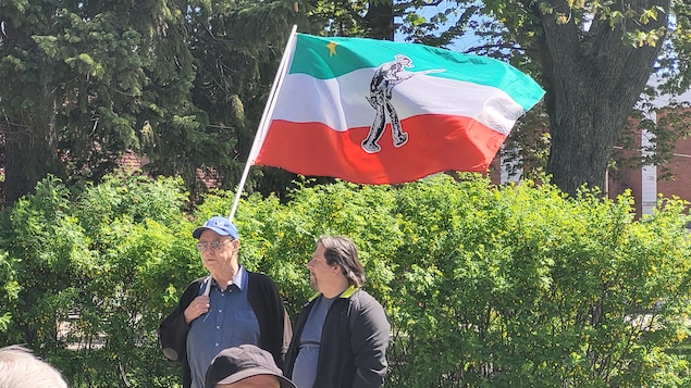 Un homme tient un drapeau des patriotes. Un autre homme est à ses côtés. 