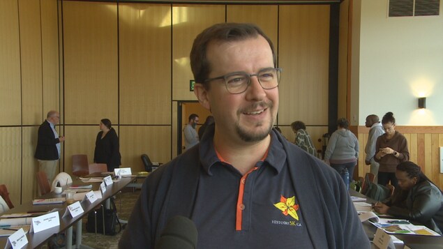 Un homme esquisse un large sourire dans une salle de conférence.