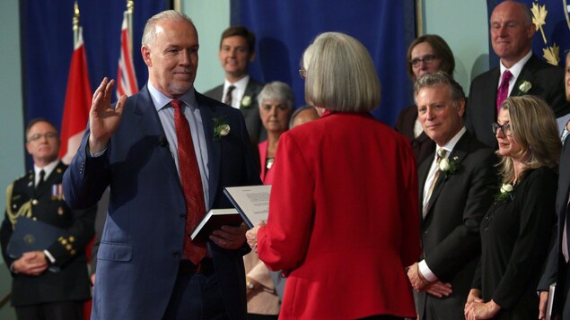 John Horgan, la main droite levée, prête assermentation devant ses ministres et la lieutenante-gouverneure Judith Guichon John Horgan, la main droite levée, prête assermentation devant ses ministres et la lieutenante-gouverneure Judith Guichon