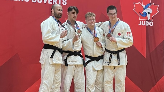 Quatre judokas ceintures noires en kimono affichent leurs médailles.