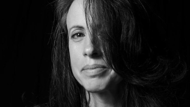 Portrait en noir et blanc, sur fond noir, de l'autrice Julie Bosman. Elle porte une veste en jean, un chandail noir, et la moitié de son visage est cachée par une mèche de cheveux.