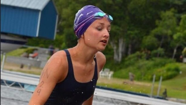 Une jeune femme en maillot de bain sort de l'eau lors d'une épreuve sportive. Une jeune femme en maillot de bain sort de l'eau lors d'une épreuve sportive.