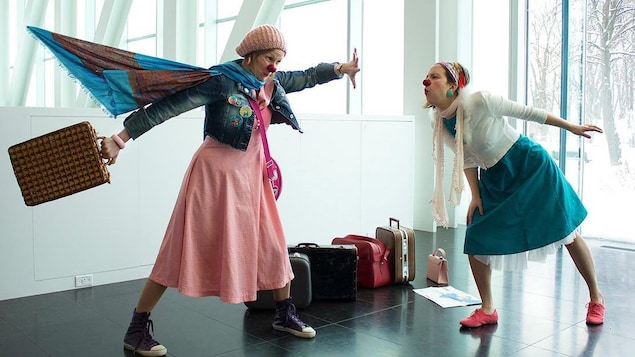 Deux femmes avec des nez de clowns font des mouvements exagérés dans un salle blanche. Dehors, c'est l'hiver. 
