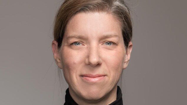 Portrait en couleur, sur fond gris, de l'autrice Julie Bouchard. Elle porte les cheveux attachés et un col roulé noir. Elle sourit légèrement, bouche fermée.