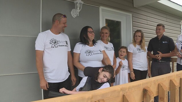 Une famille et un enfant en fauteuil roulant sur le perron d'une nouvelle maison.