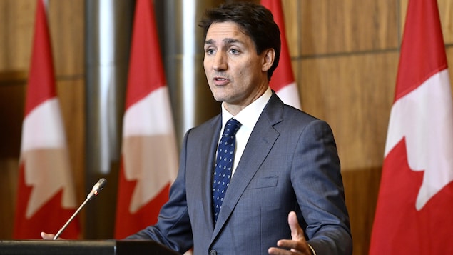 Justin Trudeau devant un micro et une tribune, s'adresse à ses interlocuteurs. 