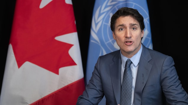 جوستان ترودو متحدثاً في مؤتمر صحفي ويبدو خلفه علما كندا والأمم المتحدة.