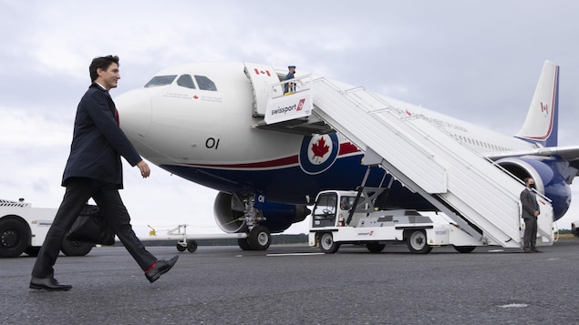 رئيس الحكومة الكندية جوستاتن ترودو يسير على مدرج المطار باتجاه سلّم طائرة بيضاء الللون عليها العلم الكندي.