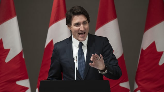 Justin Trudeau sa podium at may mga watawat ng Canada sa kanyang background.