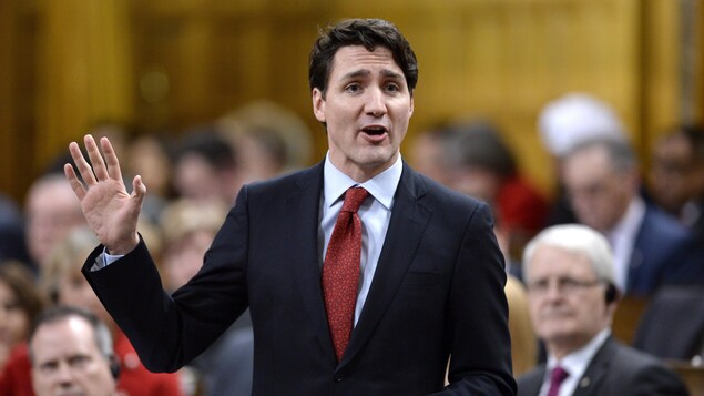 Plan moyen de Justin Trudeau, la main droite levée.