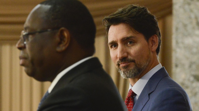 Justin Trudeau regarde vers la caméra derrière Macky Sall, vu de profil.