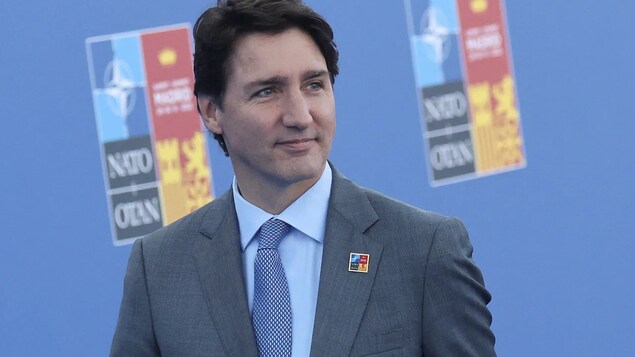 Justin Trudeau bahagyang nakangiti, makikita ang logo ng NATO summit sa background. 