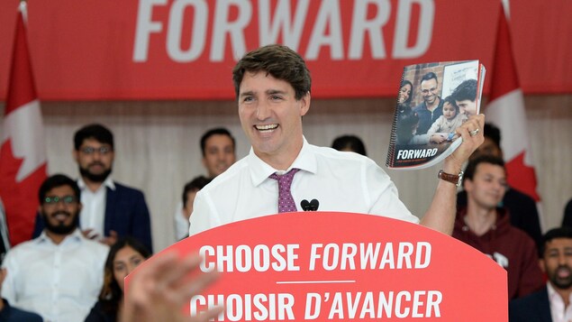 Justin Trudeau sourit. Il tient dans sa main gauche un exemplaire de la plateforme du Parti libéral du Canada.
