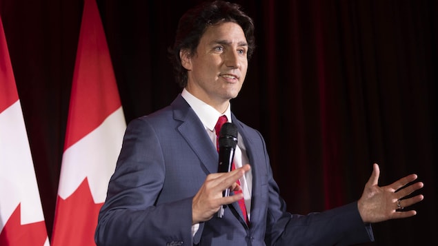 Justin Trudeau hawak ang mikropono at nagsasalita habang may watawat ng Canada sa background.