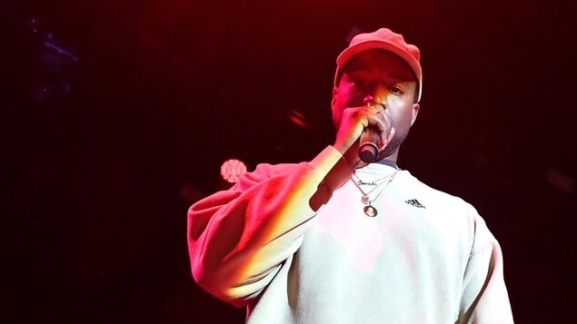 Kanye West avec un micro à la main sur scène lors d'un événement promotionnel.