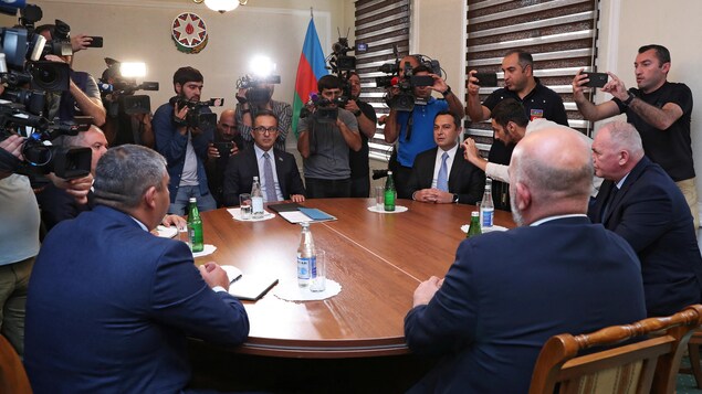 Des hommes sont assis autour d'une table avec des caméramans et des photographes autour d'eux.