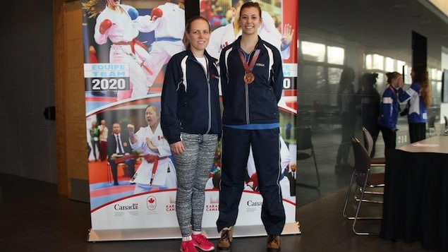 Deux femmes posent devant une affiche.