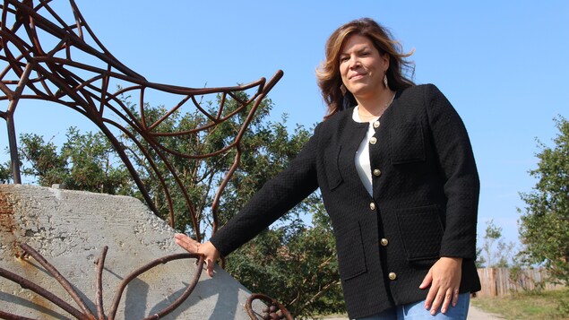 Une femme pose dehors, proche d'une sculpture de fer.