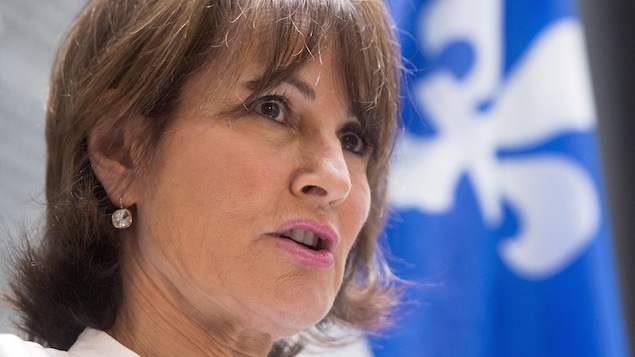 Kathleen Weil parle devant un drapeau du Québec, qui se trouve en arrière plan.