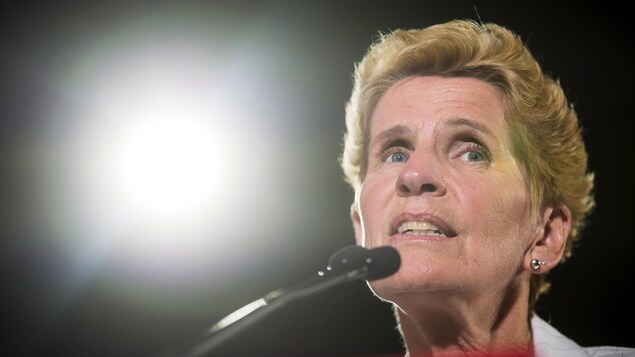 Photo de Kathleen Wynne au micro, la lumière d'un projecteur en arrière-plan Photo de Kathleen Wynne au micro, la lumière d'un projecteur en arrière-plan