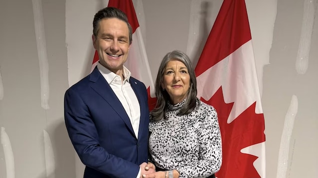 Pierre Poilievre hawak ang mga kamay ni Kathy Borrelli habang nakatayo sa harap ng watawat ng Canada.