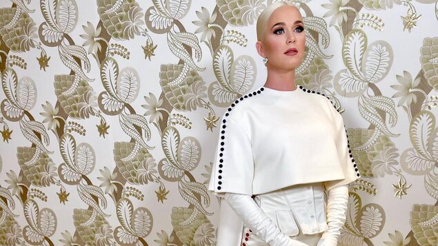 Katy Perry porte une longue robe blanche avec des boutons rouges et des boutons bleus.