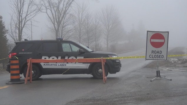 Un véhicule de police, derrière un barrage routier, une journée brumeuse.