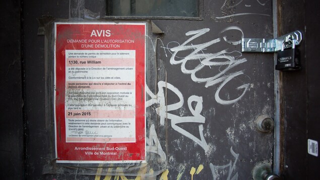 Un avis pour une demande d'autorisation de démolition d'édifice est affichée sur la porte de l'immeuble désaffecté.