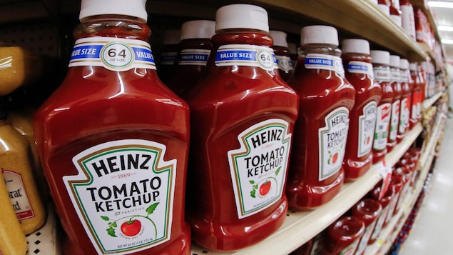 Des bouteilles de ketchup Heinz alignées sur une étagère de supermarché.