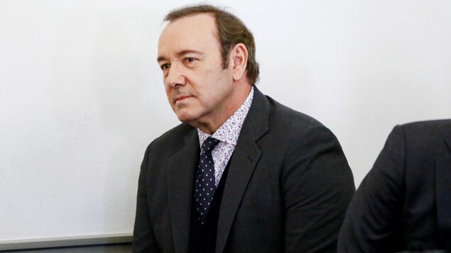 Un homme portant un costume gris et une cravate regarde devant lui. 