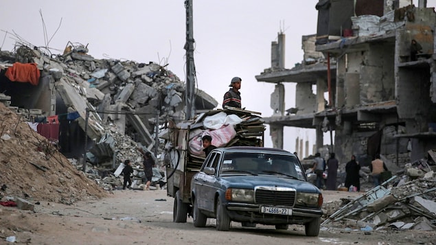 Des réfugiés sur une camionnette qui circule dans des ruines.