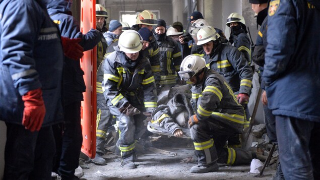 Des pompiers soulèvent une civière dans des ruines.