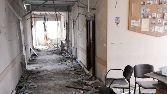 Un couloir d'hôpital endommagé à la suite de bombardements. Des chaises sont renversées sur le sol et des câbles pendent du plafond. 