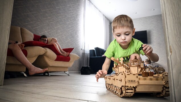 Un bambin jouant avec un char d'assaut miniature.