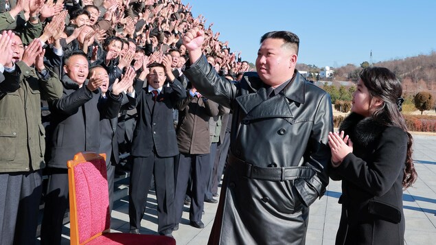 Kim Jong Un, le poing dans les airs, devant une foule d'hommes qui l'applaudient. 